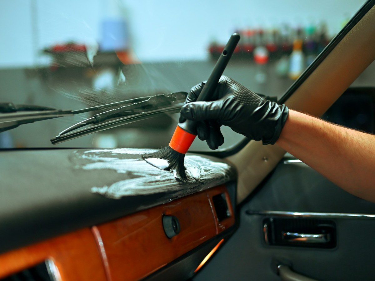 Detailer cleaning a car dashboard with a brush in the shop