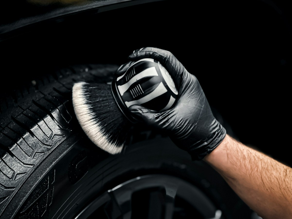 Gloved hand cleaning an alloy wheel and tire with a detailing brush